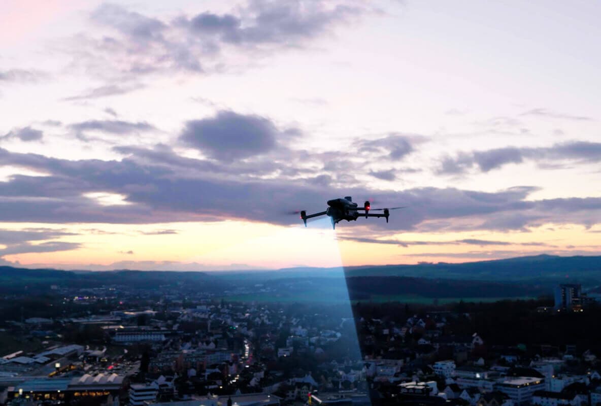 Alacakaranlıkta şehir üzerinde projektörlü drone